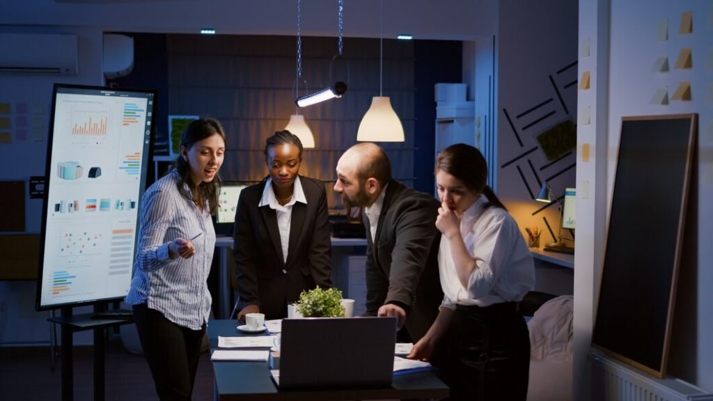 Team of business individuals engaged in work at a digital marketing company, illuminated by office lights at night.